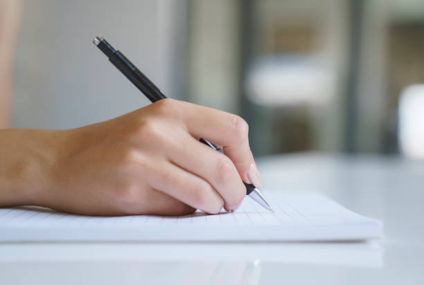 close up of a woman's hand with pen writing on a notebook - endorsing business application form filling imagens e fotografias de stock