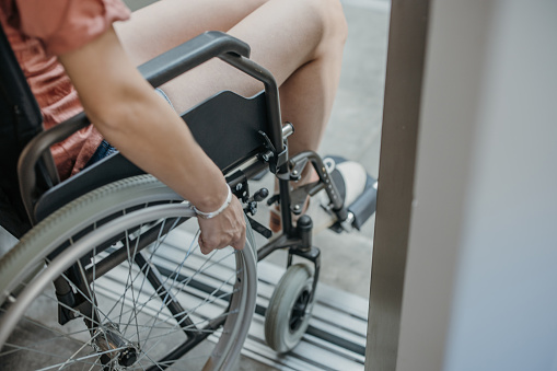 Disabled woman in wheelchair entering elevator back view. Comfortable living conditions for people with disabilities concept