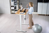 Woman Using Adjustable Height Standing Desk In Office