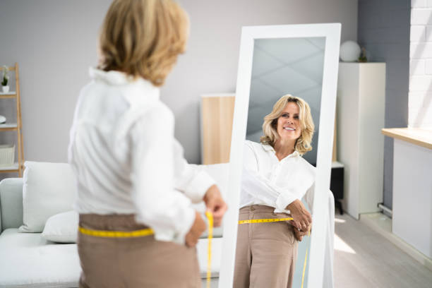 smiling slim woman looking at her reflection - mirror women looking reflection imagens e fotografias de stock