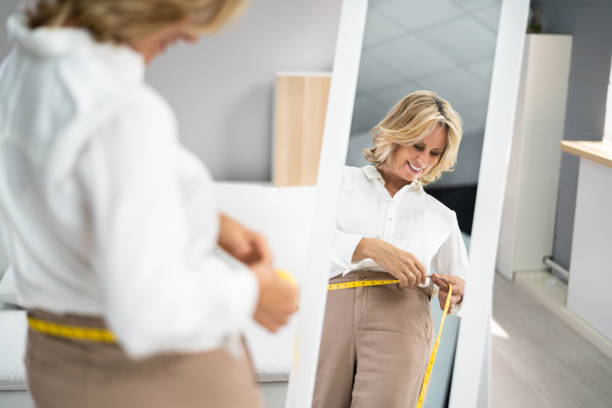 smiling slim woman looking at her reflection - mirror women looking reflection imagens e fotografias de stock