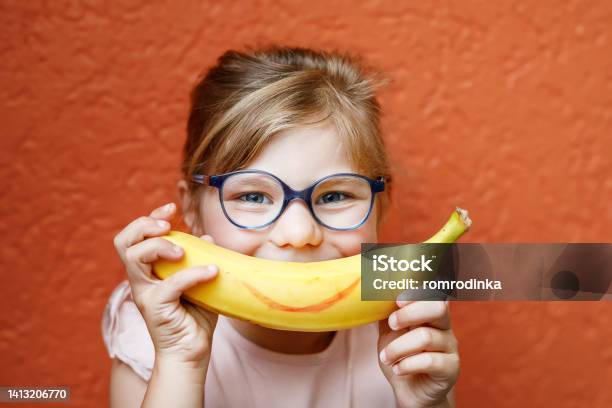 Happy Little Child Girl With Yellow Banana Like Smile On Orange Background Preschool Girl With Glasses Smiling Healthy Fruits For Children Stock Photo - Download Image Now