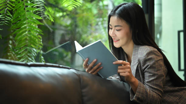 istock Relaxed working woman resting, taking a break from work and reading a book on sofa. 1413210259