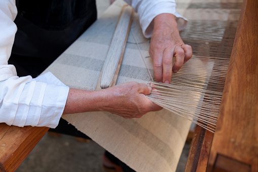 Close up on the hands of a man weaving a canvas from flax fibers with an antique hand weave machine.