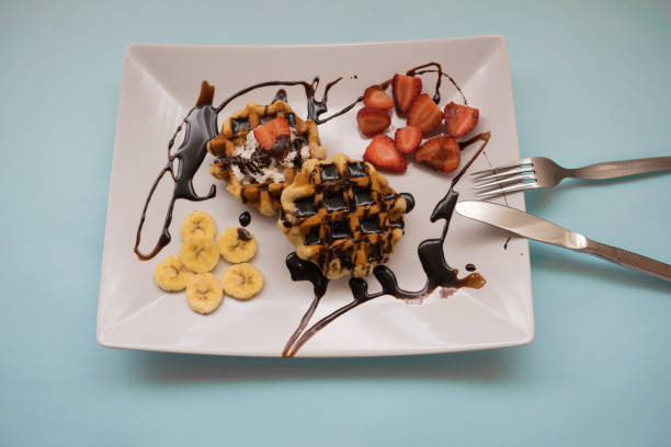 Waffles with chocolate syrup, strawberries and banana on a plate on a blue background