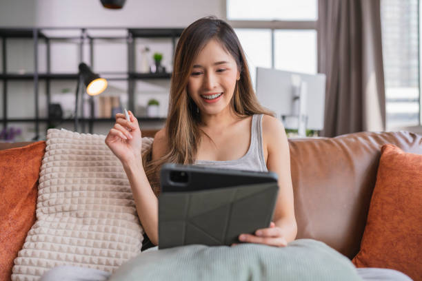 istock young attrative asian female working at home hand use tablet checking businesss data chart planning report with leisure relax on sofa in living room home isolate concept 1413222768