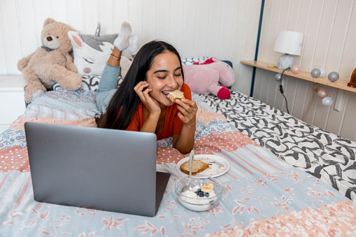 Young  Woman Snacking In Bed And Using Laptop