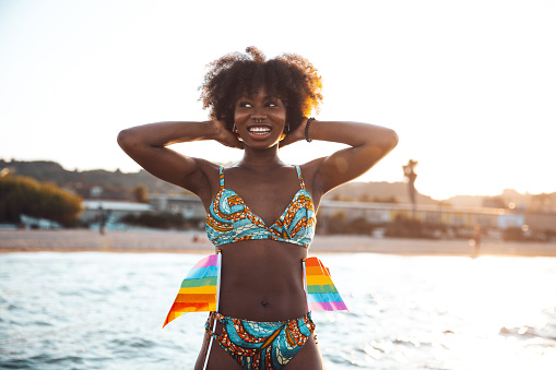 One Generation Z black woman with afro hairstyle standing for lgbtqia rights and attending to a concert-parade on the beach in summertime.