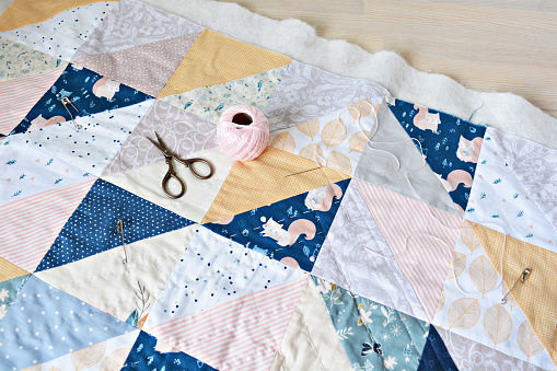 Hand stitch quilting process: cotton thread, needle and scissors on table
