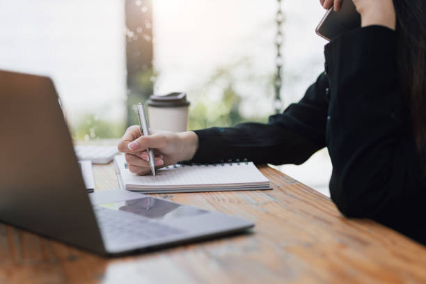 istock Asian businesswoman chatting on her mobile phone while analyzing her monthly work schedule and writing a note of an appointment with a client. 1413227042