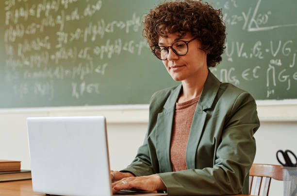 istock Young confident teacher typing on laptop keypad while sitting by workplace 1413233179