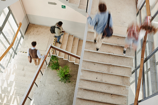 Blurry motion of multicultural teenage male and female students of highschool on staircases inside large modern university