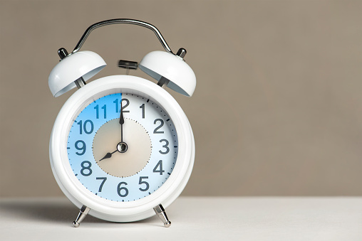 Eight o'clock on the alarm. A white alarm clock is on a white table. The clock hand points to 8 o'clock. Time to change to summer or winter time. Set an alarm for 8:00 or 20:00. copy space