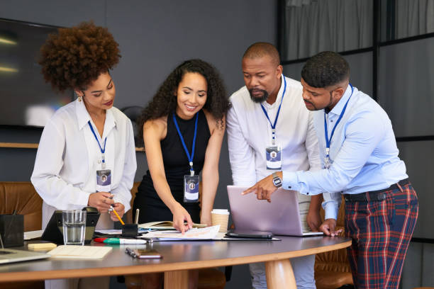 istock Confident and happy business team reading, talking about work project during a meeting while standing around office desk. Diverse group of colleagues discussing contract documents around laptop. 1413238291