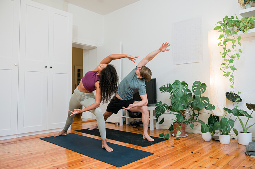 Fitness couple practicing stretching yoga at home. Man and woman standing on yoga mat and stretching in exercise room indoors.