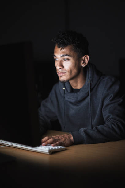 istock Young man working at a computer in a darkened office at night 1413246384