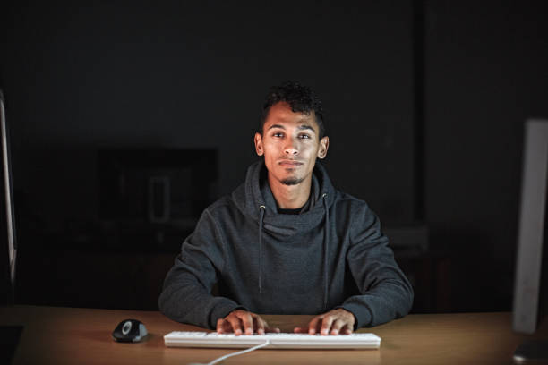 istock Young man working at a computer in a darkened office at night 1413246446
