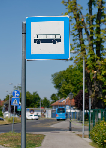 Vertical photo of a Bus stop sign on a metal pole with the street and sky in the background