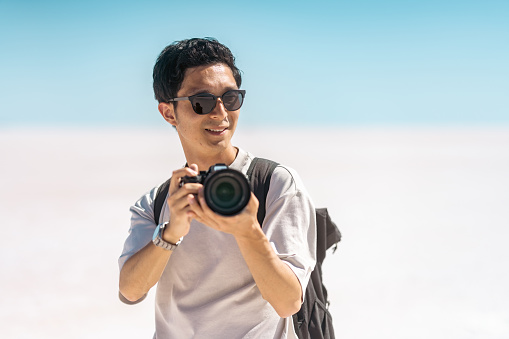 A young male tourist is taking videos and photos with his camera on white salt in Salt Lake.