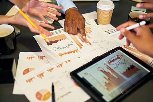 Accounting and statistics team analyzing graphs and charts on the office tablet and discussing company performance. Closeup of business analysts talking and planning the growth of a startup