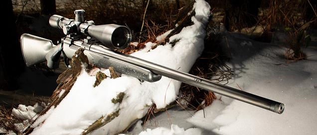 Large rifle scople and bolt action rifle on a snowy log in the forest
