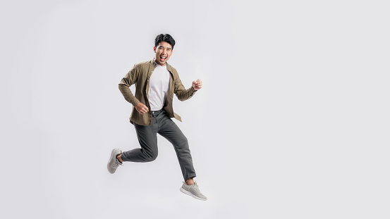 Full length handsome Asian man happy smile and looking at camera he is run in air on isolated white background. Cool man joyful running in copy space. Studio short.