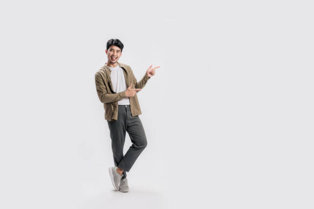 Full length smart young Asian man happy smile standing hand pointing to empty space on white background.