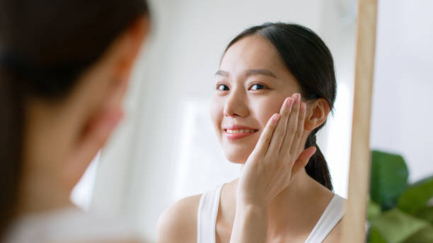 Young Asian beautiful woman touching healthy facial skin look at mirror, Asian beauty skin concept stock photo
