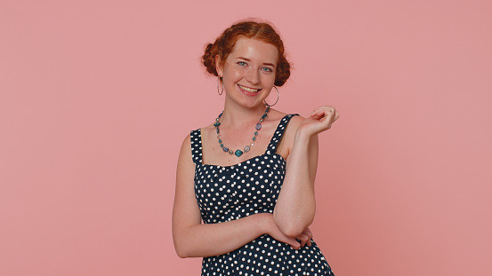 Cheerful lovely redhead young woman in black dress smiling, looking at camera, flirting. Adult fashion red hair model girl indoors studio shot isolated on pink background. Female nature beauty