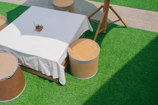 Sunlight and shadow on surface of outdoors wooden dining table set made from waste materials with patio umbrella on artificial turf, high angle view with copy space