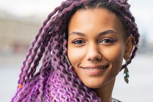 afro hairstyle, colored hair, purple curls, African woman with wavy kanekalon on her head, violet braids, professional braiding