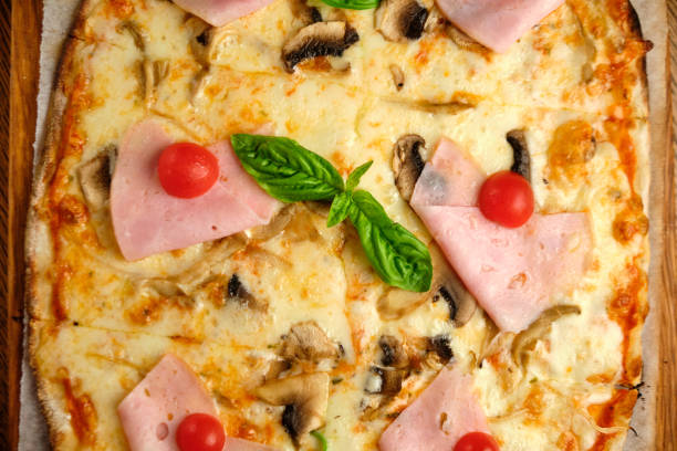 Pizza on a rustic baking paper, served on a kitchen or restaurant table, with fresh vegetables, herbs and spices, representing a wellbeing and indulgence in food, city life and modern culture lifestyle, street food culture
