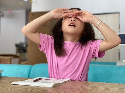Asian little girl rubs her eyes with hands to relieve fatigue