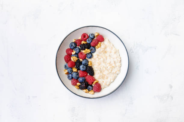 Bowl of oatmeal porridge with blueberry and raspberry on white table top view. Yummy and diet breakfast. stock photo
