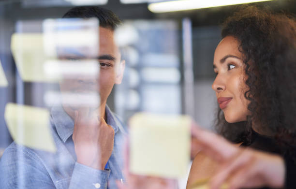 istock Business teamwork planning a strategy while working with sticky notes on a glass wall in the boardroom. Colleagues or coworkers meeting, discussing and brainstorming in their office 1413269411