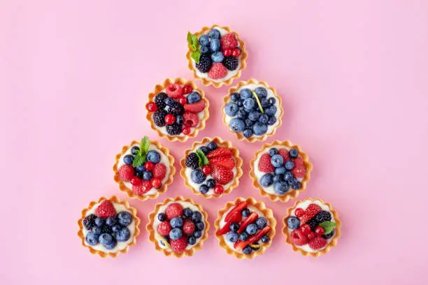 Set of different tartlets or cake with cream cheese, honey and summer berry on pink. Pastry dessert from above. Flat lay style.