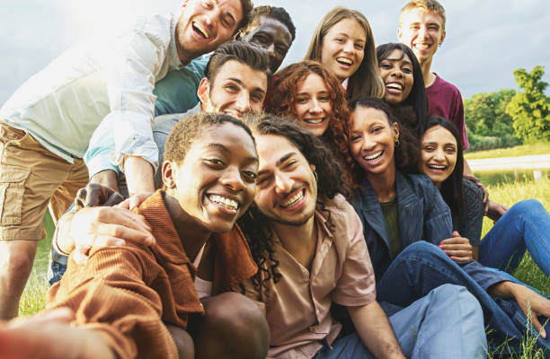 Cheerful international happy friends having fun taking selfies at picnic in the countryside - Large group of multiethnic young people smiling looking at the camera - focus on the black woman face Cheerful international happy friends having fun taking selfies at picnic in the countryside - Large group of multiethnic young people smiling looking at the camera - focus on the black woman face international match stock pictures, royalty-free photos & images