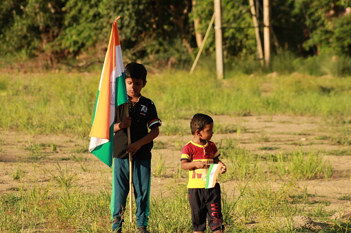 little Boy holding tri colour national Indian flag in the nature & waving flag in the air. Independence Day - Holiday and Republic Day