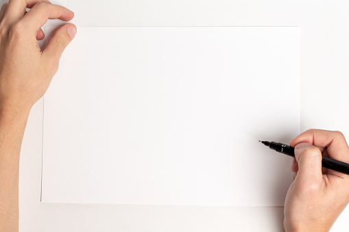 Photo of an empty sheet of paper with human hand holding a pen and copy space