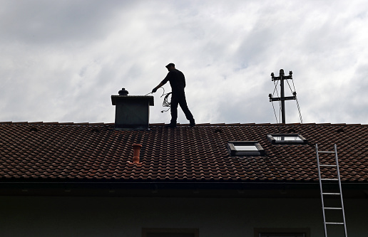 A chimney sweep cleans the chimney on a house roof