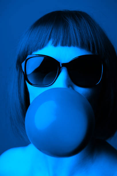 istock Woman with sunglasses blowing chewing gum bubble studio portrait 1413283696
