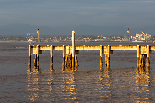 Late afternoon sun shines on Pier at Mukilteo Ferry Terminal. In background city of Everett WA.