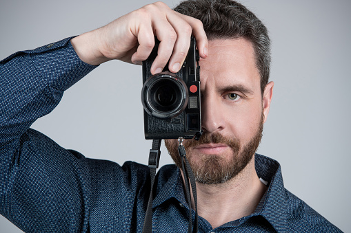 Middle-aged photographer take photograph looking in eye of handheld photo camera grey background, snapshot.