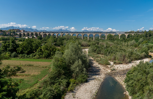 Cuneo, Piedmont, Italy - August 06, 2022: The Soleri viaduct, it is a promiscuous road and rail bridge on the Stura di Demonte river, in the background the mountains of the Alps