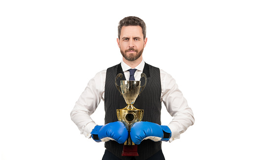 Businessman in suit, no tie, holds 3D trophy award object in his hand in front of blue technological background with large copy space. Business and Finance Concept.