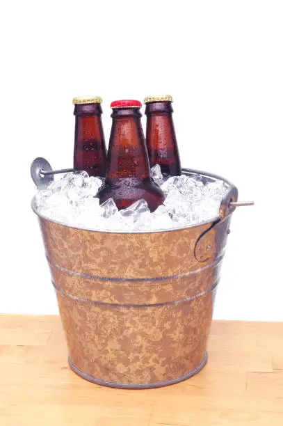 Three Beer Bottles in Metal Bucket on Wood Table and White Background