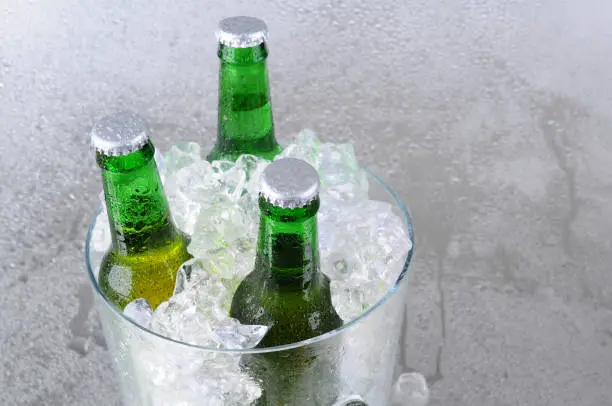 Three green beer bottles in a crystal ice bucket. High angle with copy space to the right side. Horizontal format.