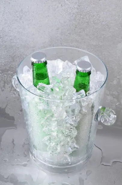 Two green beer bottles in a crystal ice bucket sitting on a wet stainless steel surface. Vertical Format with shallow depth of field.