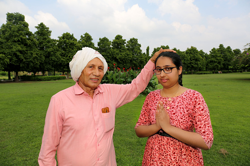 Grandfather giving blessing to his granddaughter portrait together outdoor in park.