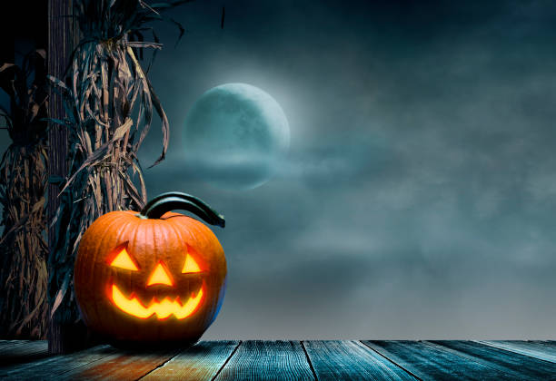 Jack O'Lantern Sits On Porch In Front Of Corn Stalks And Rising Moon stock photo